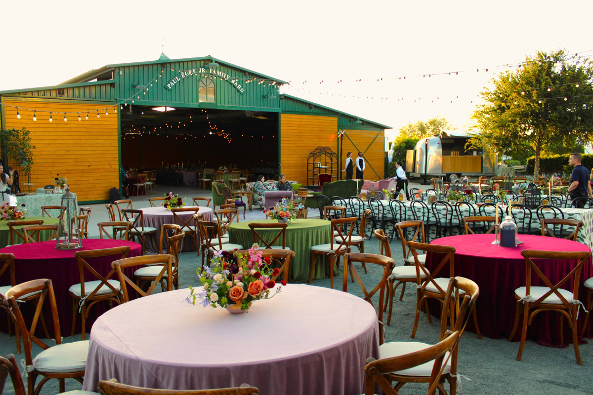 The Paul Ecke Jr. Family Barn at the Flower Fields Carlsbad set up for an event, with round tables covered in pink linens and string lights hanging overhead.