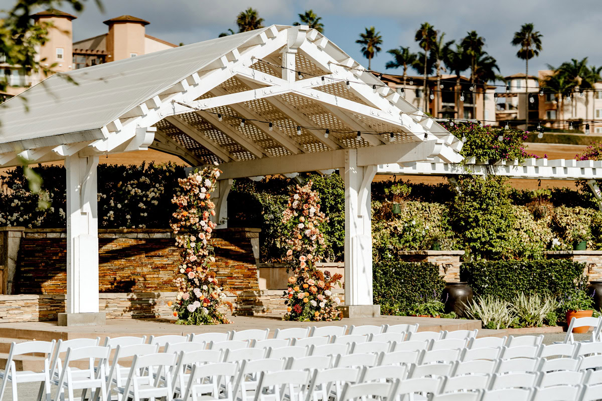 Event hall at The Flower Fields Carlsbad decorated with flowers on the pillars and many white chairs.